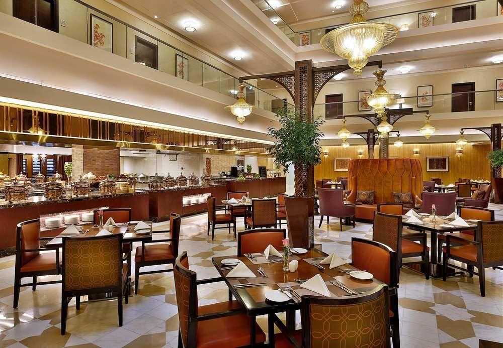 Jabal Omar Marriott Hotel Makkah La Meca Exterior foto The photo shows the interior of an elegantly decorated restaurant. It features comfortable seating arrangements with wooden tables and chairs, some adorned with white tablecloths and neatly arranged cutlery. The space is well-lit, with stylish light 