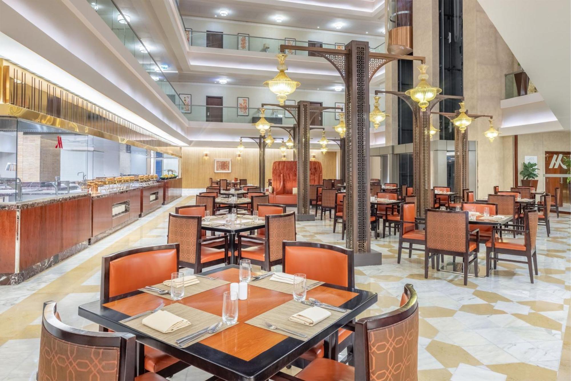Jabal Omar Marriott Hotel Makkah La Meca Exterior foto The photo depicts an elegant dining area within a restaurant. The space features several tables, each set with plates, glasses, and napkins. The seating consists of brown chairs with orange accents. The restaurant has a modern design, highlighted by 